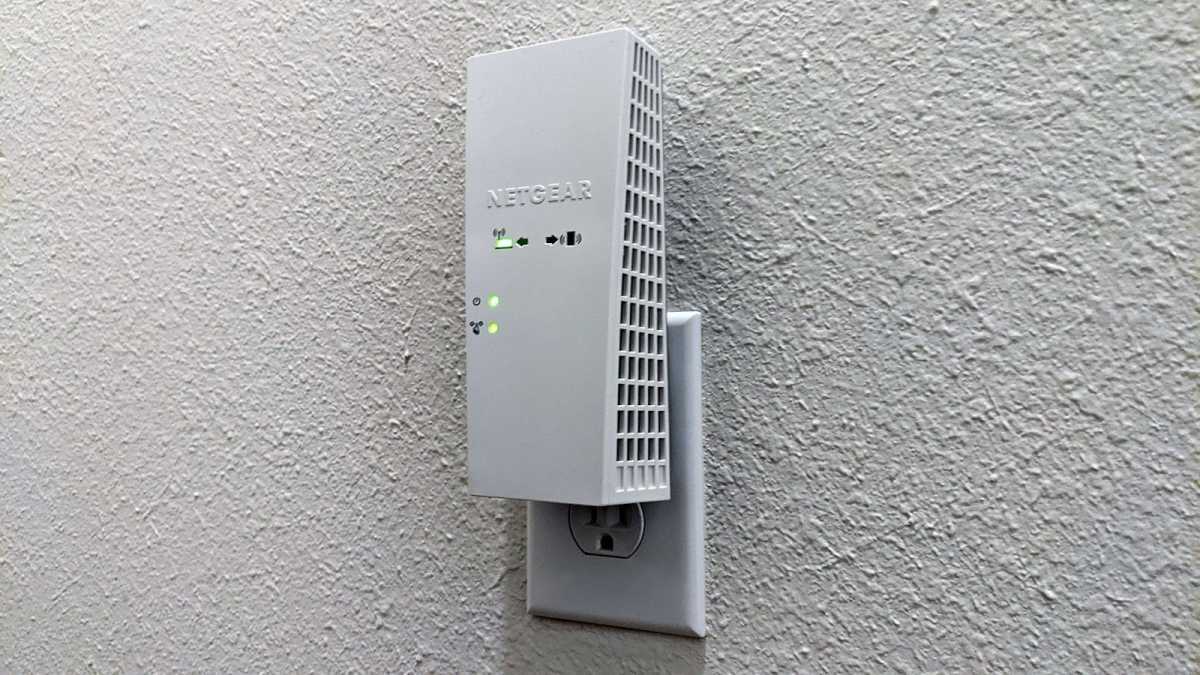 A Netgear Wi-Fi extender plugged into a wall outlet on a white wall