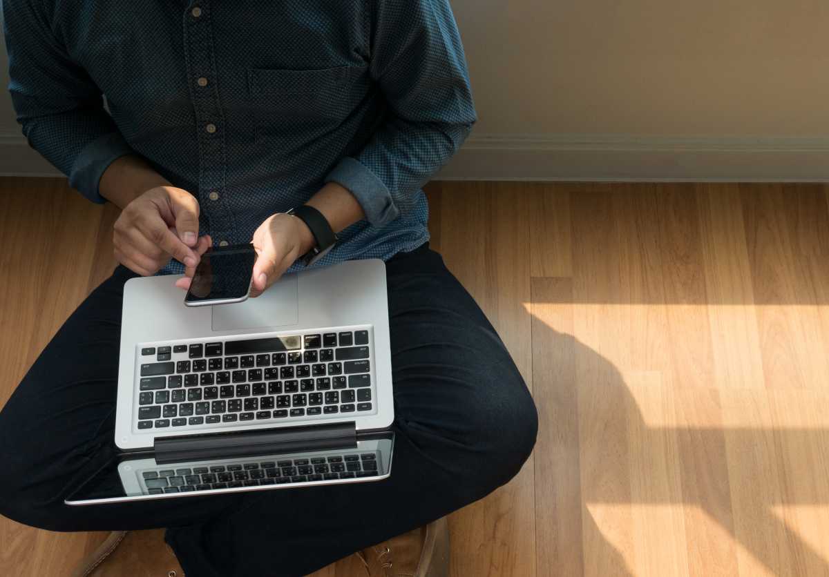 hombre usando iPhone con MacBook en su regazo