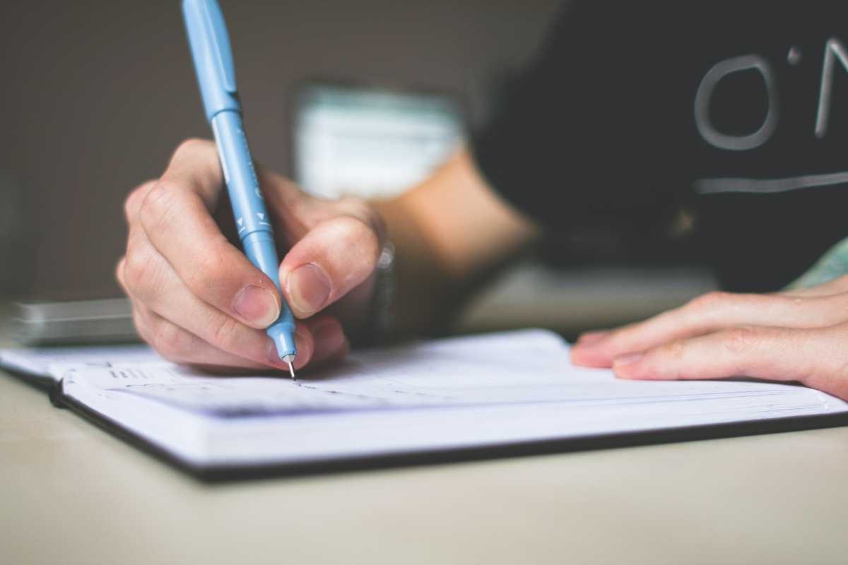 Person holding a blue pen over a notebook, ready to write