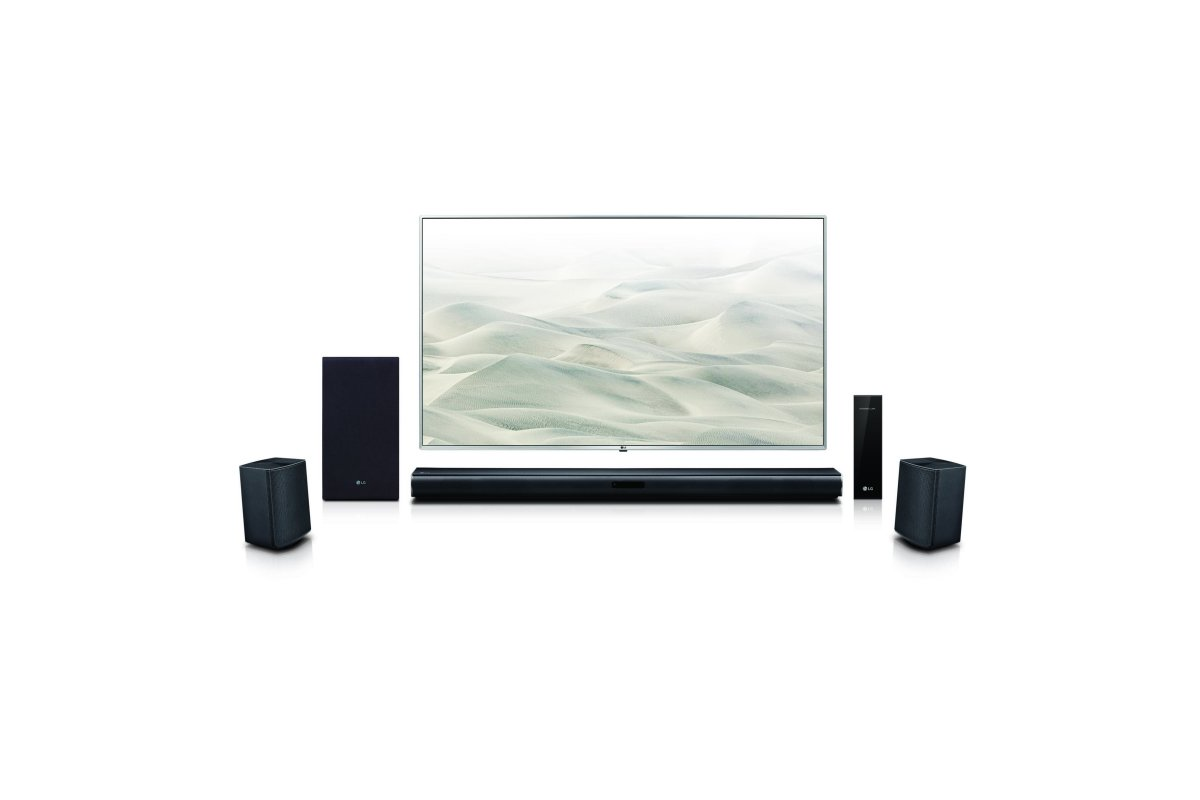 an LG soundbar in front of a tv showing sand dunes with four other speakers surrounding them