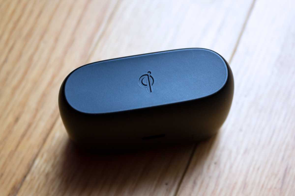 Jabra 85t charging case on a wood floor, with the bottom facing up and showing the Qi wireless charging symbol