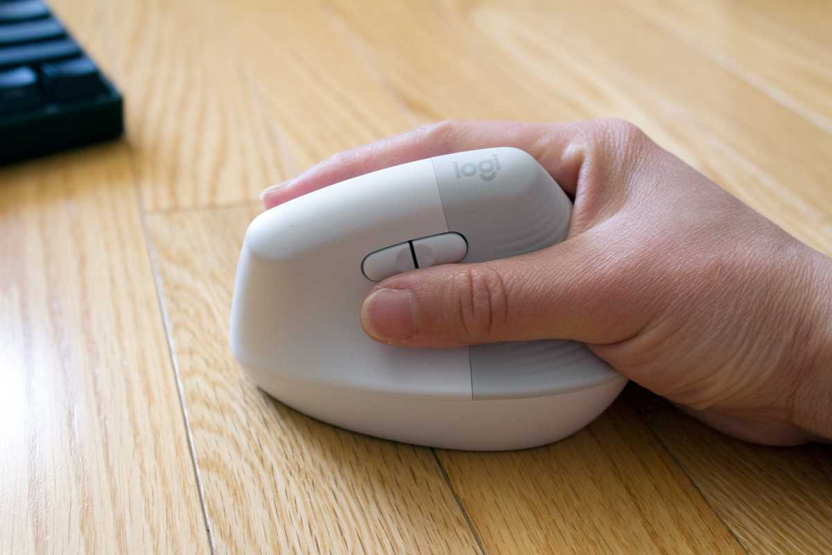 A hand holding a Logitech Lift mouse with a black keyboard in the background