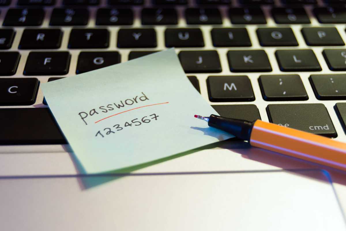 Laptop with pen and a post-it showing a weak password lying on top