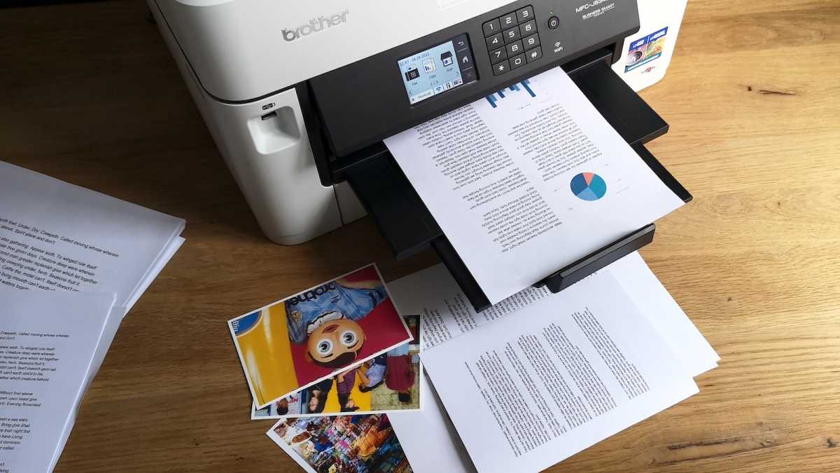 Documents containing text, pie charts, and bar graphs on A4 plain paper, and colour photographs printed on glossy 4x6in photo paper strewn around the Brother MFC-J5340DW inkjet printer