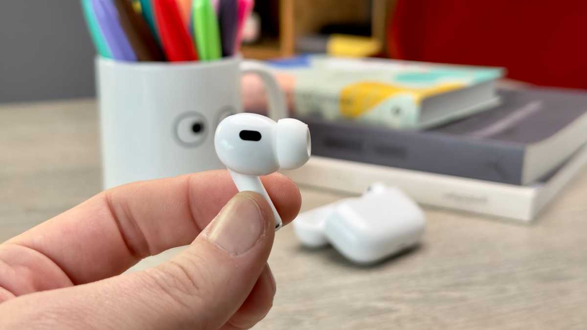 Holding the AirPods Pro (2022) earbud with case in the background