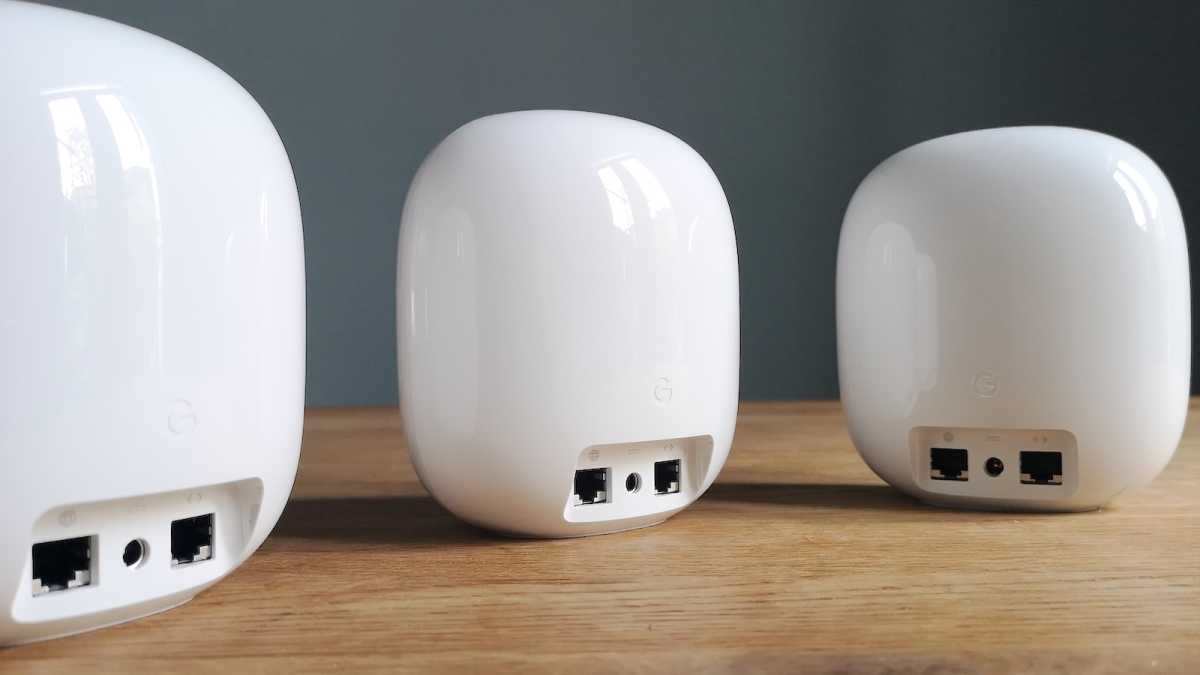 Three Google Nest WiFi Pro devices on a tabletop, their Ethernet ports and mains power sockets facing forwards.