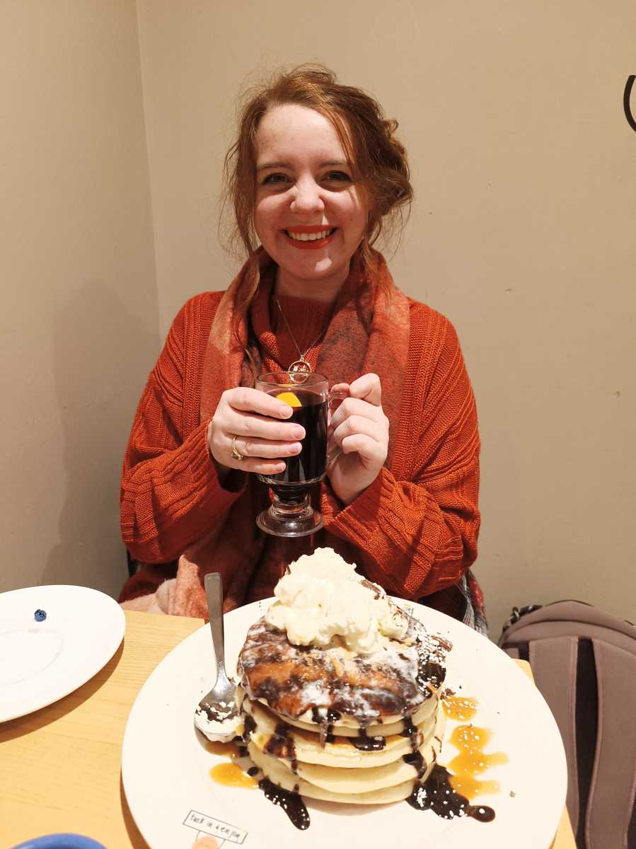 Woman holding mulled win and eating pancakes