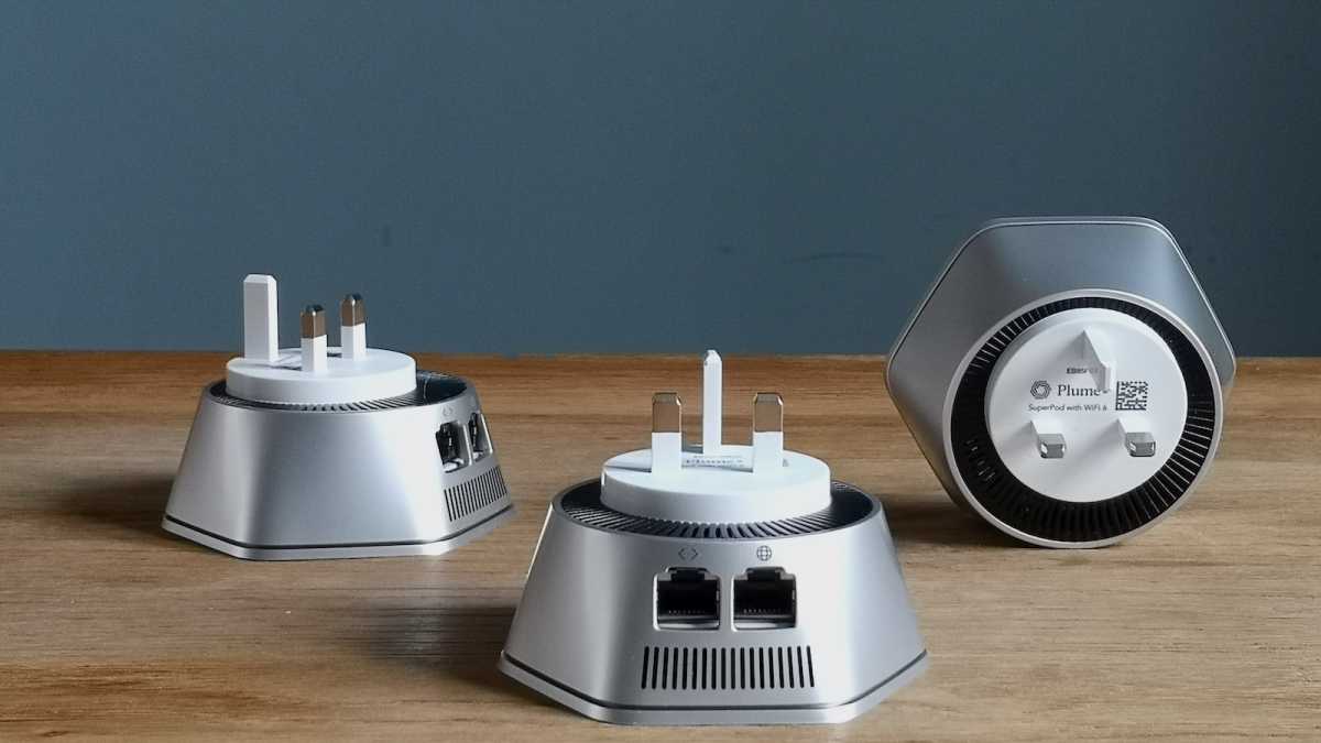 Three Plume SuperPod Wi-Fi 6 units on a table, with the Ethernet ports and UK mains adapter prongs visible