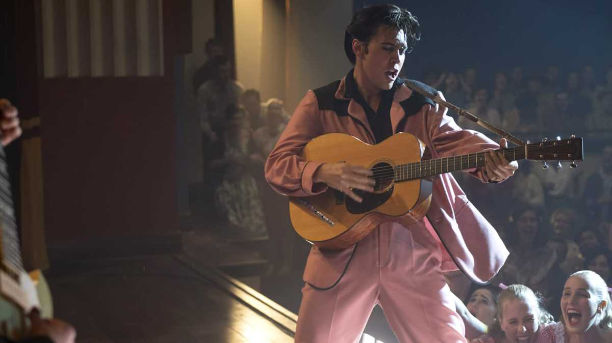 Austin Butler como Elvis Presley, vestido com um terno rosa segurando um violão