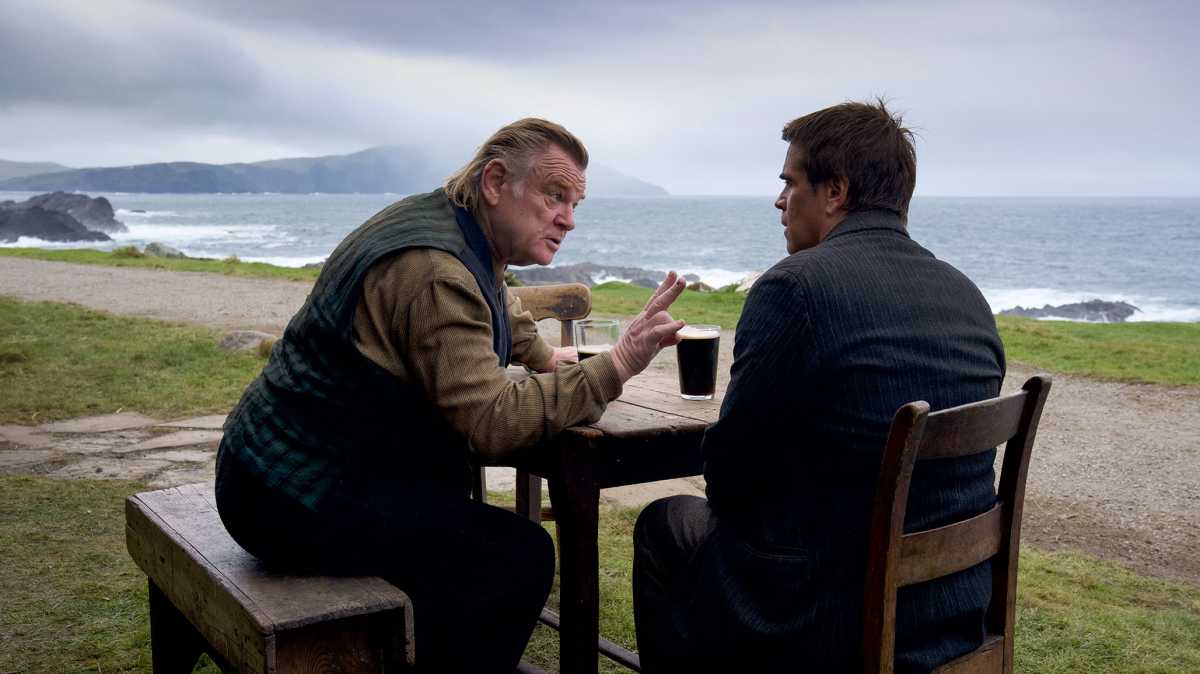 The Banshees of Inisherin - Colin Farrell and Brendan Gleeson sat at a table drinking Guiness on a beach