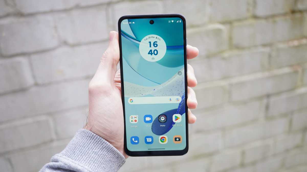 Motorola Moto G53 5G in hand with brick wall behind