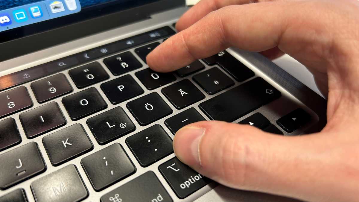 Nahaufnahme der Tastatur eines Macbook Pro, auf der Option- und der Ü-Taste liegen Finger