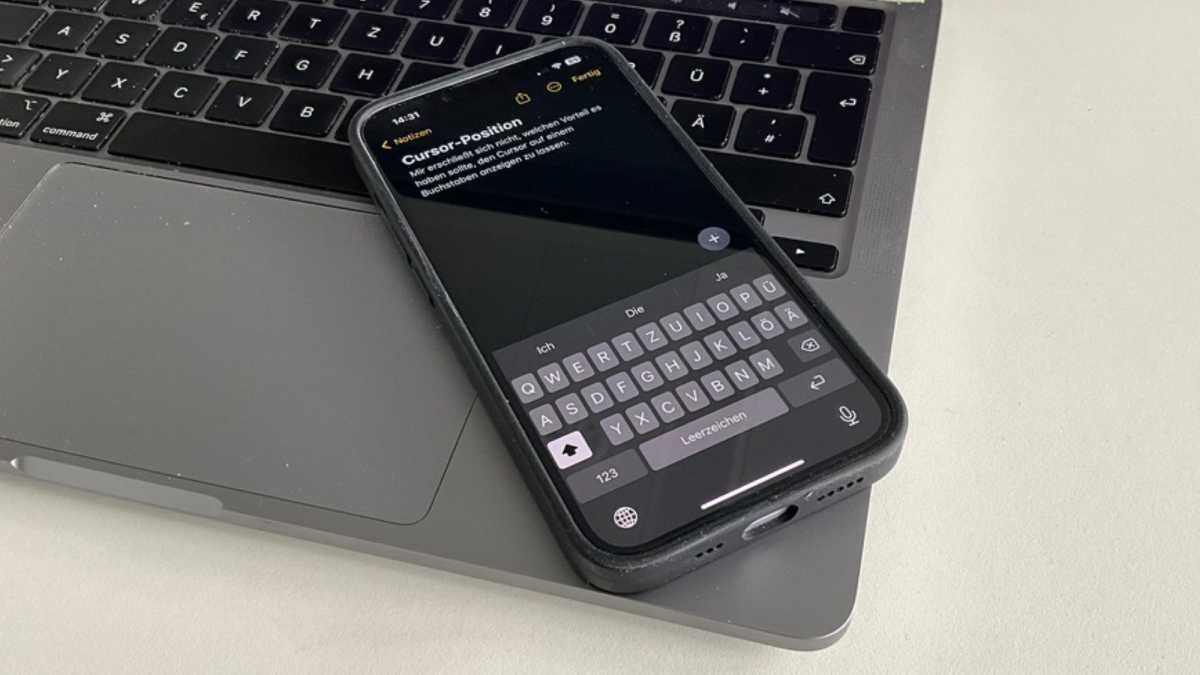 Ein iPhone 14 liegt auf einem Macbook Pro, auf dem Bildschirm ist die Notizen-App und die Tastatur zu sehen.