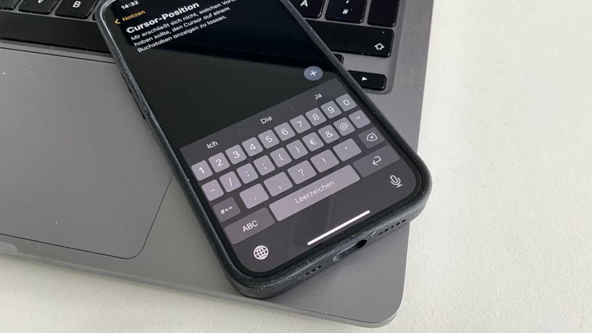 Ein iPhone 14 liegt auf einem Macbook Pro, auf dem Bildschirm ist die Notizen-App und die Tastatur zu sehen.