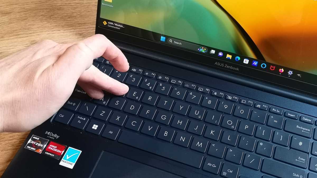 A hand pressing the W and A keys of the Asus Zenbook 15 OLED laptop