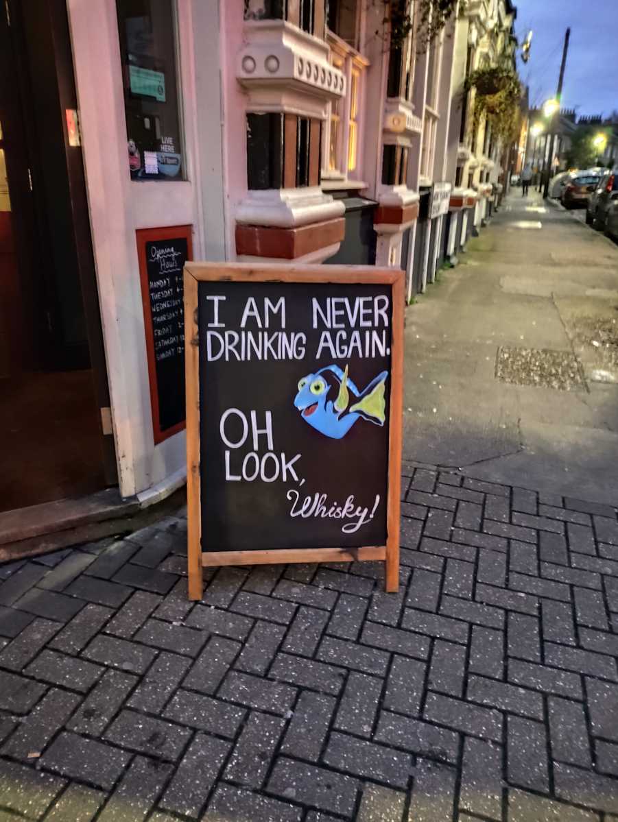 Sign saying "i'm never drinking again... oh look, whisky!' outside of a pub on a street at night