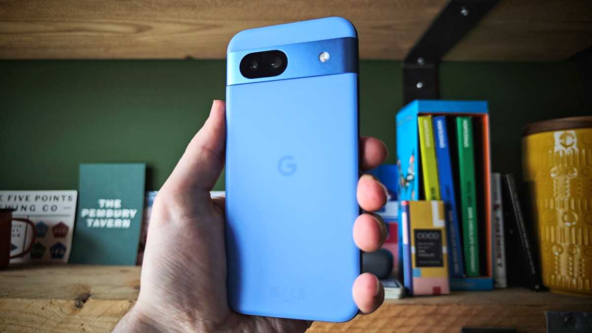 Pixel 8a in blue, held in front of a shelf