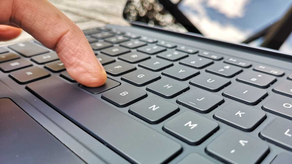 Close up of a left middle finger depressing the 'V' key on the Xiaomi Touchpad Keyboard 