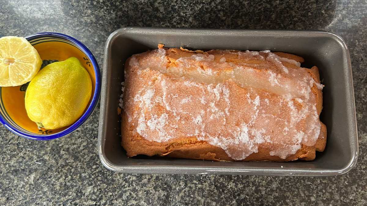 Lemon drizzle cake in a loaf tin, with a bowl of lemons beside it