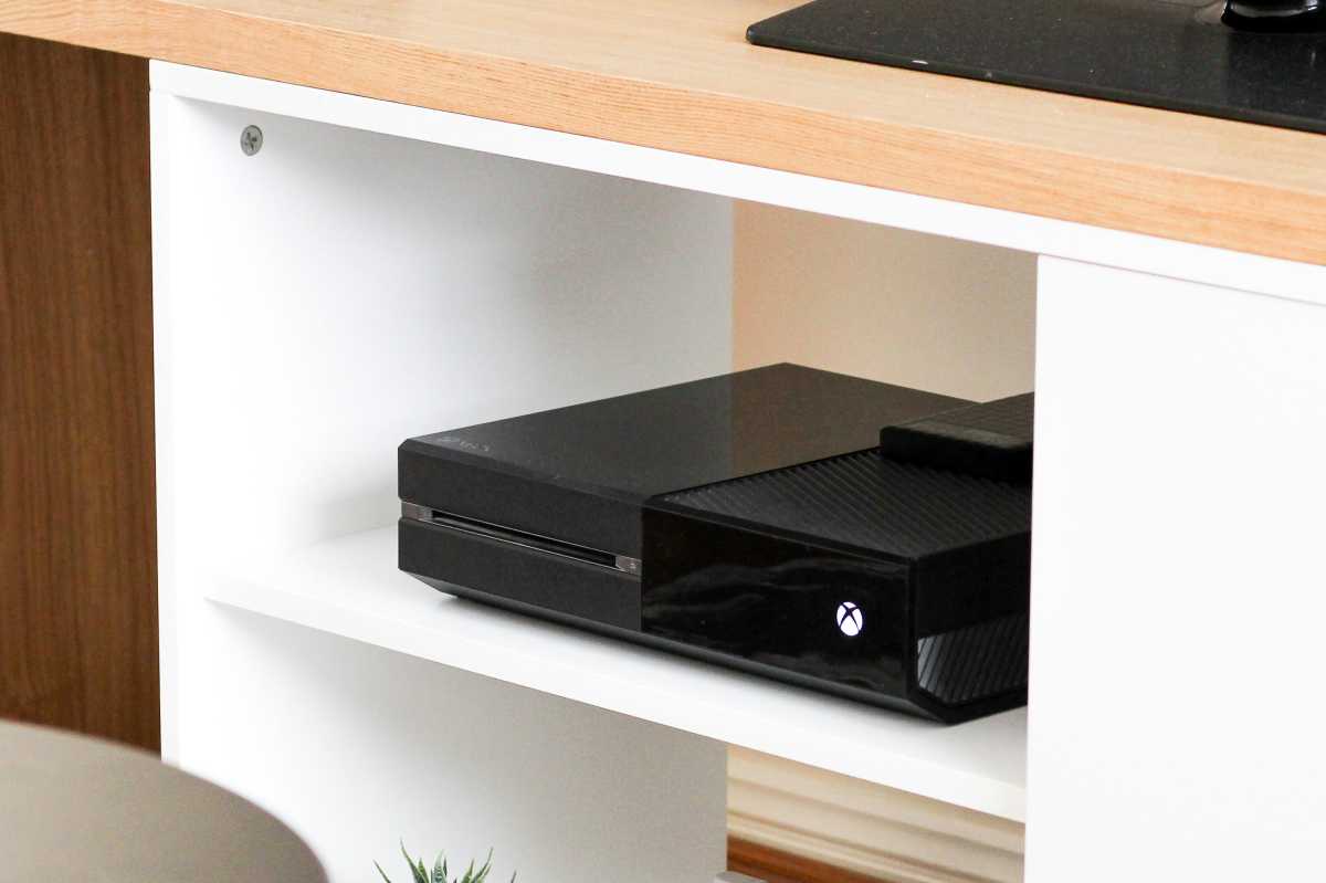 Black Xbox One on a white shelf under a TV