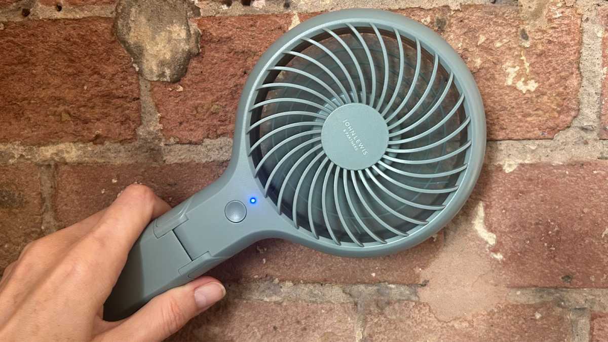 A John Lewis Anyday fan in one hand, held in front of a brick wall