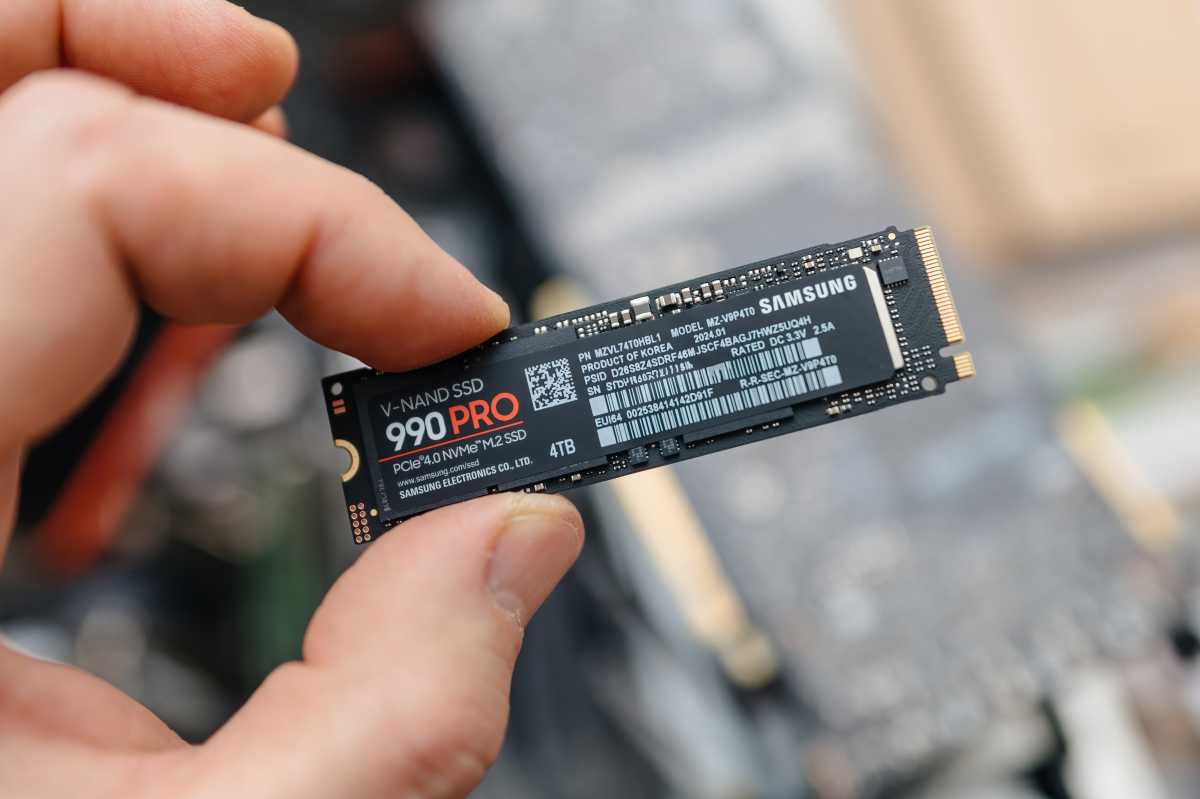 Man holding Samsung 990 PRO SSD between fingers over exposed laptop hero