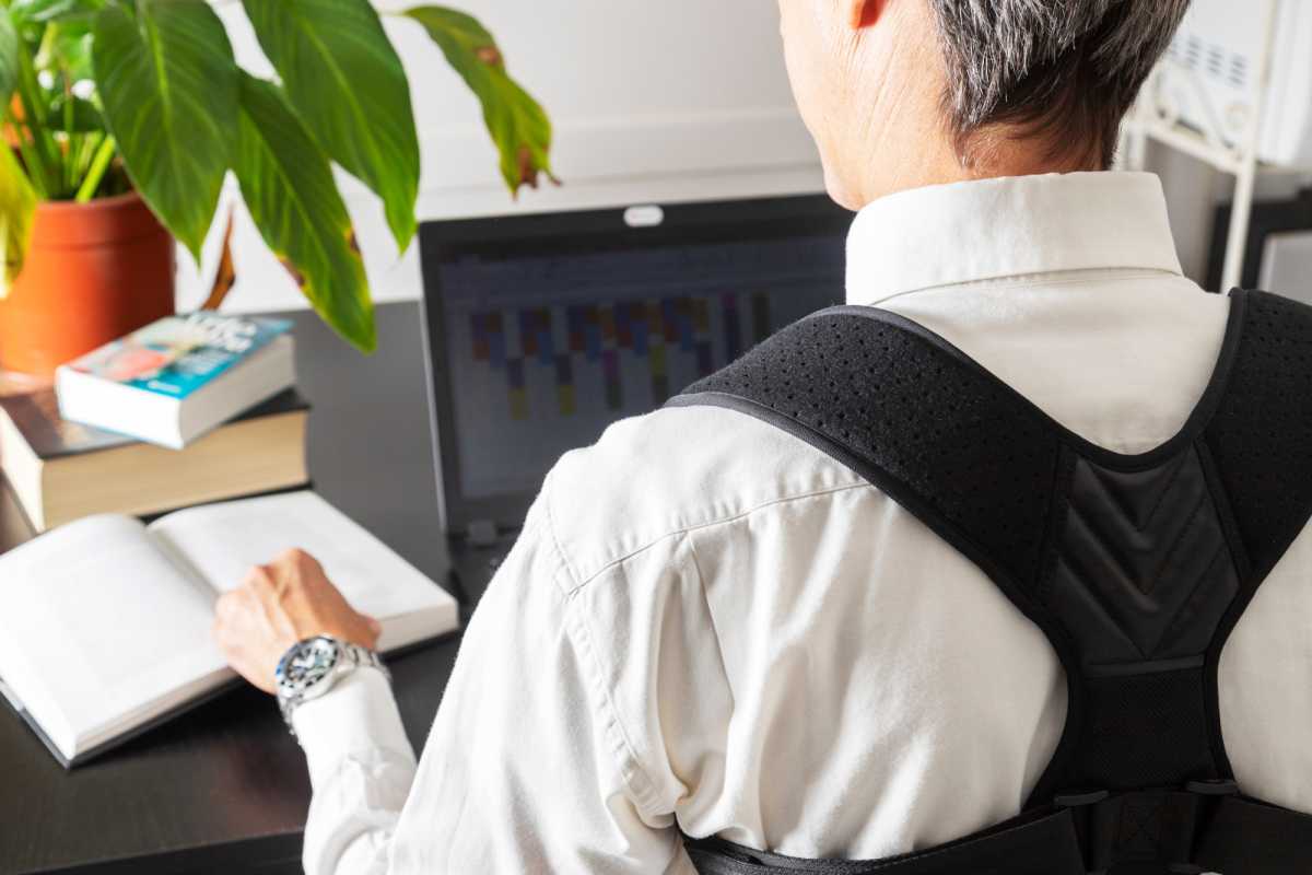 Hombre vestido con una correa correctora de postura mientras trabaja en su computadora portátil