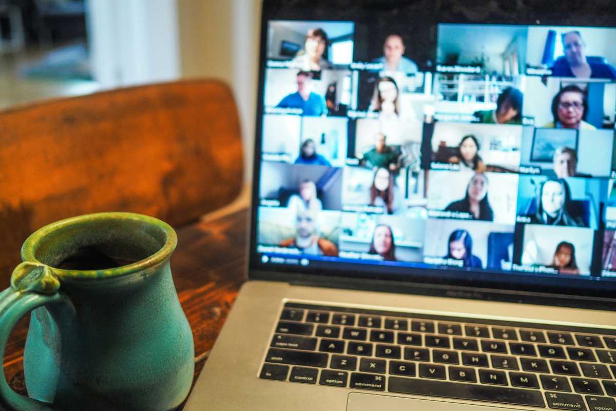 Zoom video conference call on MacBook laptop screen with mug beside