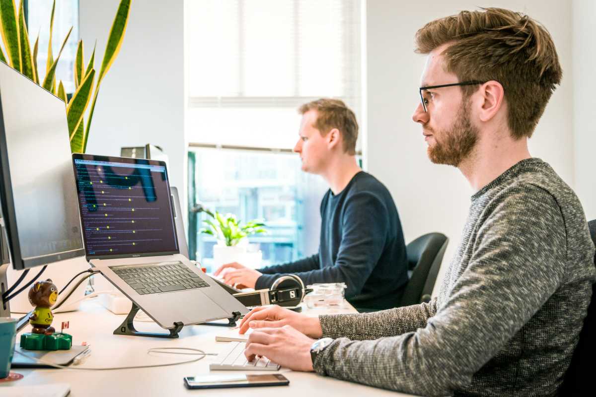 Man and his coworker both sitting at an office desk doing work on PC