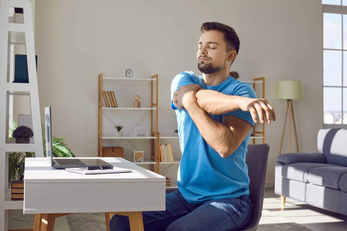 Man stretching his arms while working on his laptop at his desk