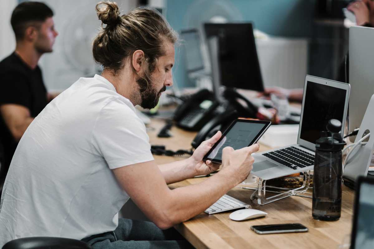 Man with bun sitting in office chair slouched over desk while working on a tablet