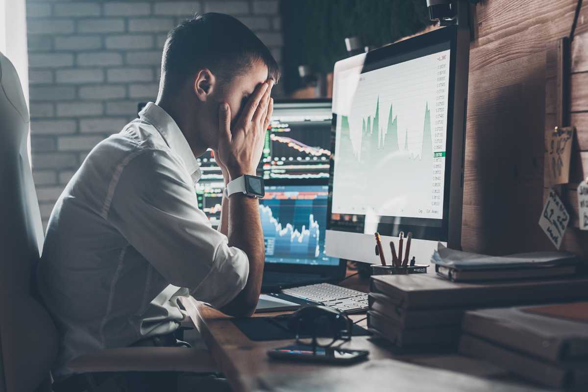 Office worker man holding head in hands at computer with sore eyes