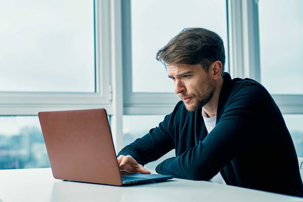 Man working on laptop on white desk in room with huge windows and natural light