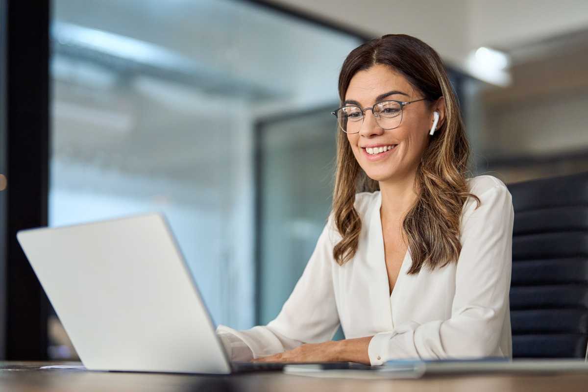 Woman working on laptop at desk while wearing white earbuds