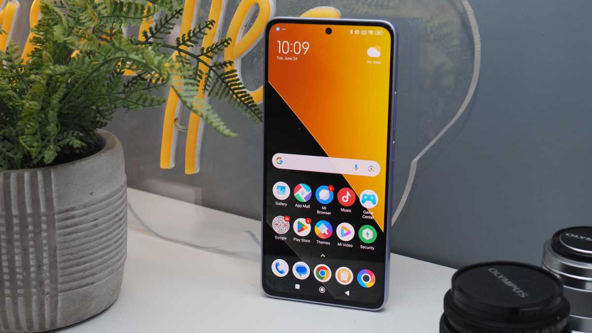 A photo of the Poco M7 Pro against a neutral backrground on a wooden shelf