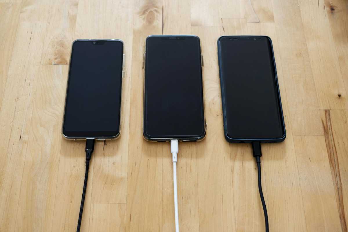 Three mobile phones with charging wires, side by side