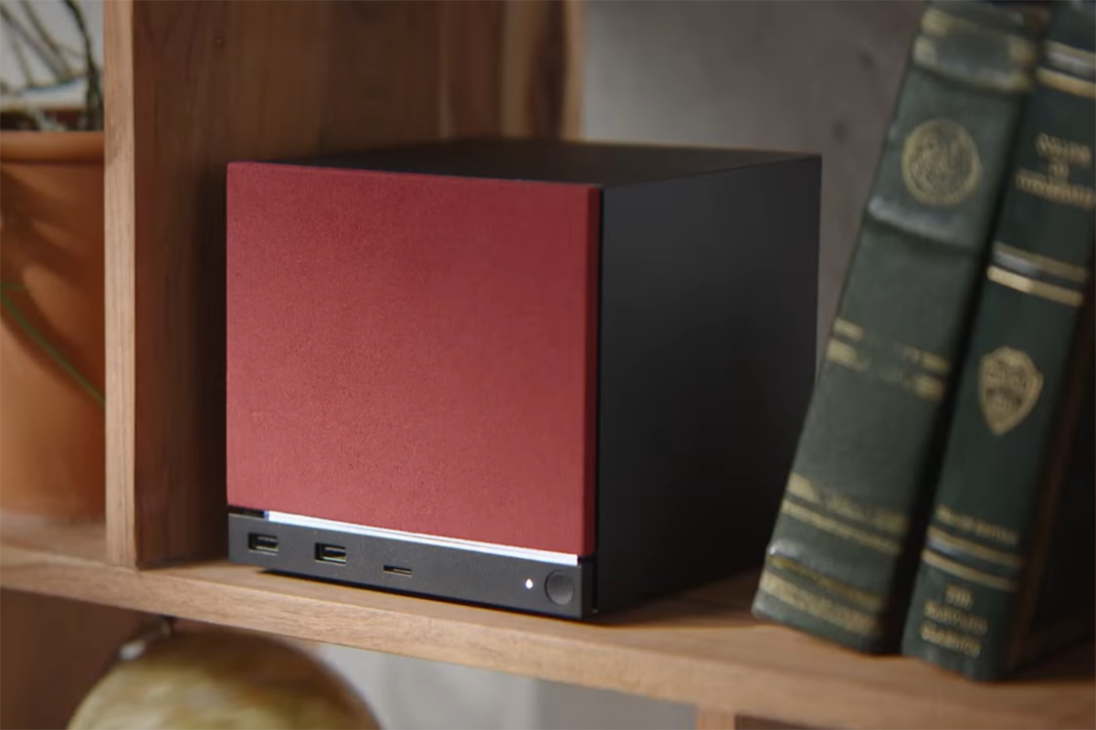 Steam Machine (2026) with red color faceplate on a bookshelf with two green books to its right