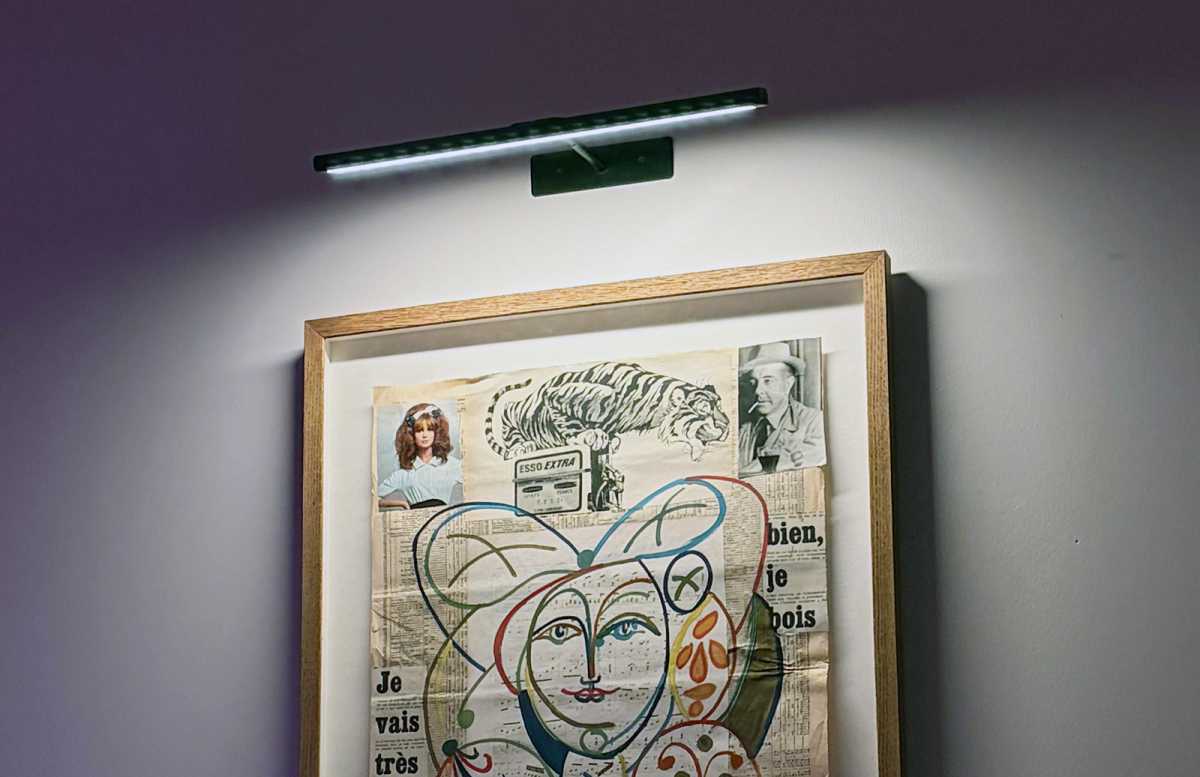 The Ezvalo Picture Light shines light down on a framed piece of artwork, hanging on a wall.