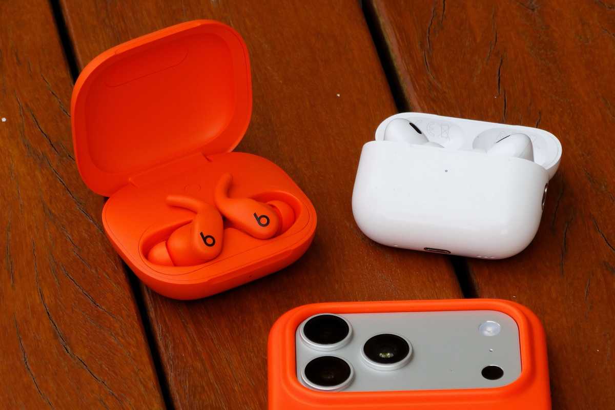 Sierra Orange Powerbeats Fit in the charging case next to AirPods Pro and an iPhone 17 Pro Max