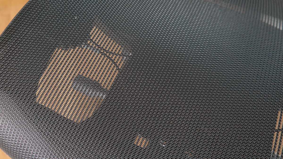 Nahaufnahme eines schwarzen Netzstoffs am Stuhl, durch den Sonnenlicht fällt.