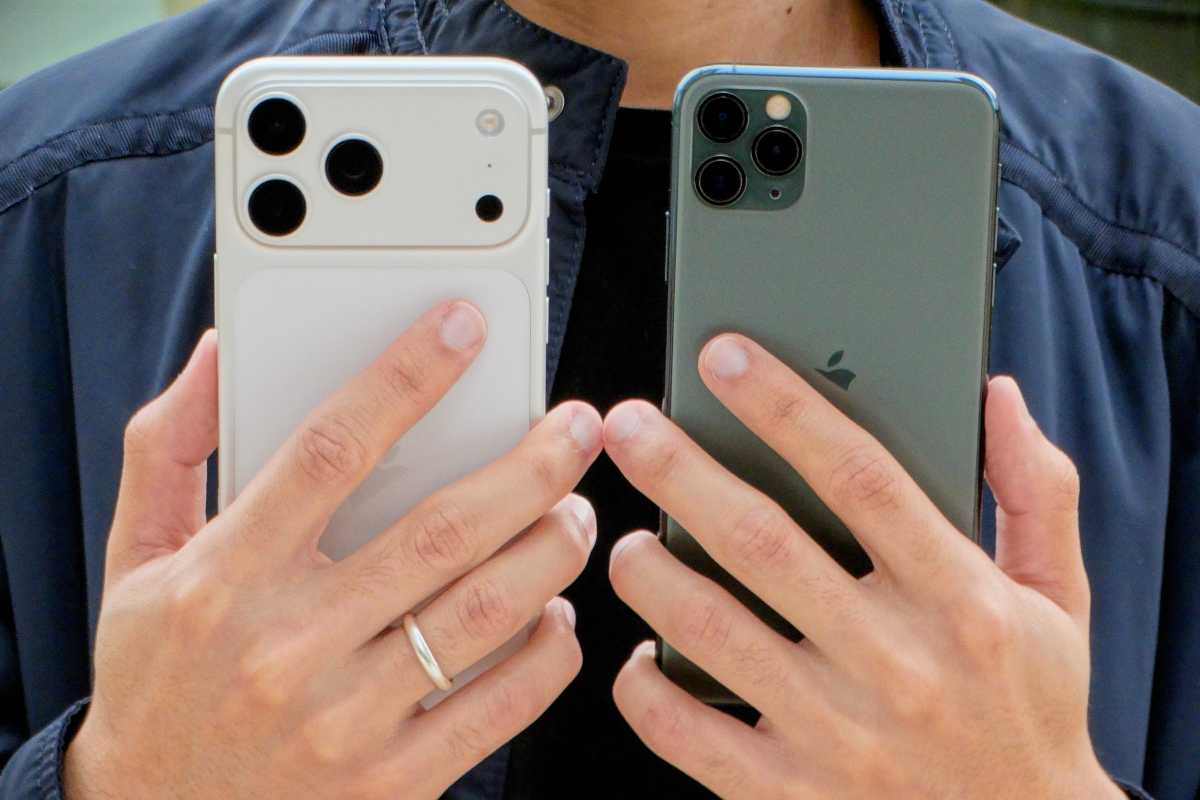 holding an iPhone 17 pro Max (left) and iPhone 11 Pro Max showing their rear cameras