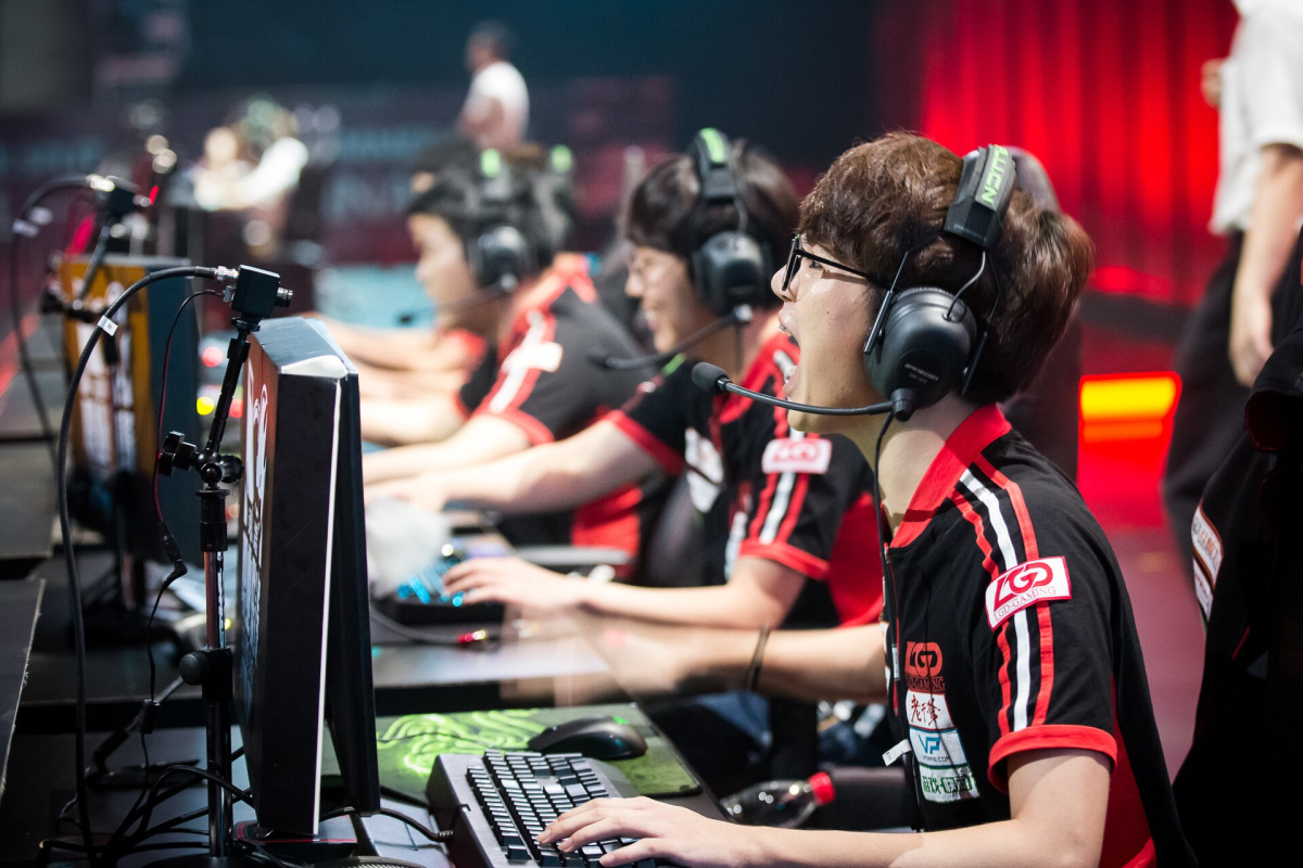 League of Legends professional tournament: A young person in a headset screams at a PC monitor, with other players behind them.